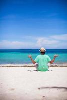 Young man sitting in lotus position on white tropical beach