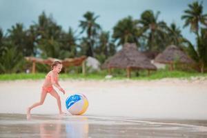 Little girl playing with big air ball on white beach photo