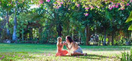 Little girl with mother sitting in the lush garden and enjoy summer rest photo