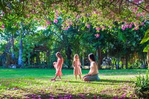 Young mother with her little daughters sitting in the lush garden and enjoy summer rest photo