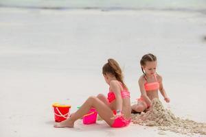 Happy little girls playing on beach sand during tropical vacation photo