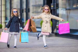 Little fashion girl with shopping bags outdoors in big city photo