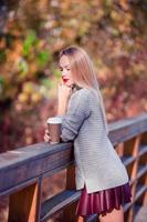 Fall concept - beautiful woman drinking coffee in autumn park under fall foliage photo