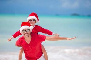 niña y padre feliz en sombrero de santa durante las vacaciones de navidad en la playa foto