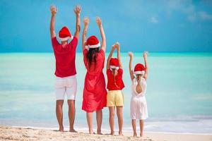 familia feliz con sombreros rojos de santa en una playa tropical celebrando las vacaciones de navidad foto