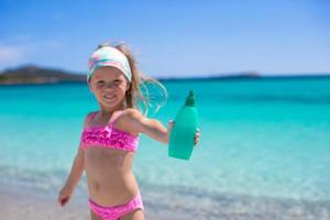 Little adorable girl in swimsuit with suntan lotion bottle photo