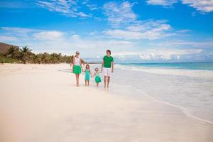 Young beautiful family of four walking on the white sandy beach photo