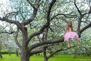 Little adorable girl sitting on blossoming apple tree photo