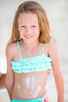 Little girl having fun at tropical beach on lounger with smile painting by suncream photo