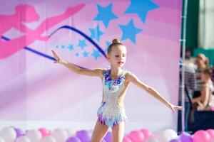 Little beautiful gymnast on carpet. Adorable gymnast participates in competitions in rhythmic gymnastics photo