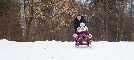 niña y padre feliz paseando en trineo en un día nevado de invierno foto