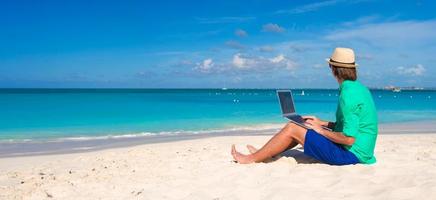 Young man working on laptop at tropical beach photo