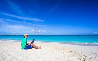 Young man working on laptop at tropical beach photo