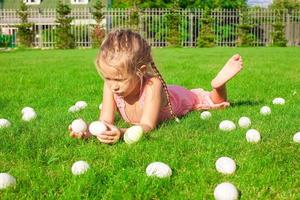 Little happy girl playing with white Easter eggs on green grass photo