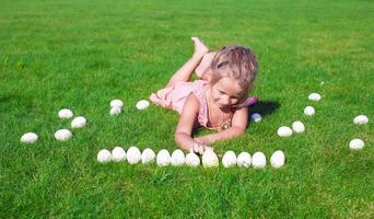 Little adorable girl playing with white Easter eggs in the yard photo