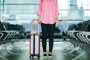 Pasajero de avión de primer plano y equipaje rosa en un salón del aeropuerto esperando el avión de vuelo. mujer joven en el aeropuerto internacional caminando con su equipaje foto