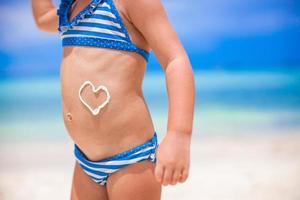 Close-up heart painted by sun cream on little girl stomach photo