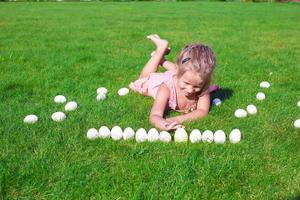 Little happy girl playing with white Easter eggs on green grass photo