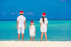 familia joven con sombreros de santa relajándose en la playa tropical durante las vacaciones de navidad foto