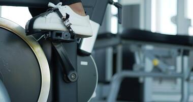 mise au point sélective, jambes d'une jeune machine à vélo tournante féminine dans la salle de sport pour l'entraînement, jeune femme faisant de l'exercice avec un simulateur de vélo à air tournant pour la santé cardiologique video