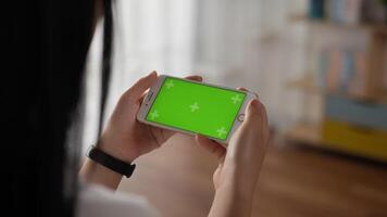 Closeup horizontal of hand woman holding smartphone with green screen while lying on couch. Blank digital smartphone in hand girl. Showing content videos blogs on center screen.