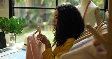 Handheld shot, young asian designer taking beautiful pink clothes from hanger and using tape measure to check neatness, startup small business entrepreneur concept video