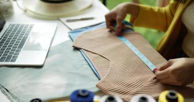 toma de mano, manos de un joven diseñador asiático usando cinta métrica para verificar el tamaño de la ropa en la mesa, concepto de emprendedor de pequeñas empresas