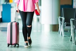 primer pasajero de avión con pasaportes y tarjeta de embarque y equipaje rosa en un salón del aeropuerto. mujer joven en el aeropuerto internacional caminando con su equipaje. foto