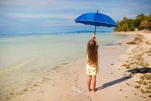 Little cute girl with big blue umbrella walking on a tropical beach photo