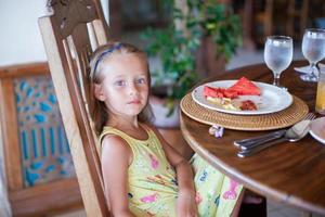 Adorable little girl having breakfast at resort restaurant photo