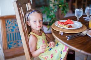 Adorable little girl having breakfast at resort restaurant photo