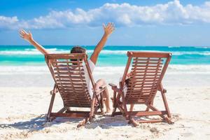 Young father with little daughter in beach chairs raised their hands up on shore ocean photo