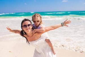 Young beautiful mother and adorable little daughter spread her arms like a bird on white beach photo