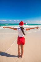 Young woman in Santa Hat walking spread her hands on white sandy beach photo