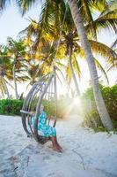 Adorable little girl in a dress and sunglasses on swing at white sandy Caribbean beach photo