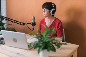 Mature woman making podcast recording for her online show. Attractive business woman using headphones front of microphone for a radio broadcast photo