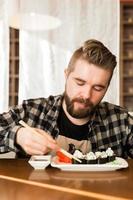 Man eating sushi rolls in a restaurant. Guy eating japanese cuisine using bamboo sticks. Culture and food and tradition in modern world photo
