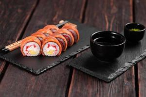 Sushi roll philadelphia with salmon and avocado and cream cheese, caviar on black background close-up. Sushi menu. Japanese food concept photo