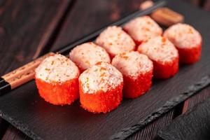 Sushi roll with mayonnaise sauce and red tobiko caviar served on black board and soy sauce. photo