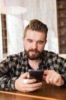 joven hipster que busca noticias de las redes sociales leídas a través de un teléfono inteligente en el tiempo libre en el café