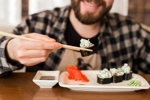 primer plano de rollos de sushi en una mesa en un restaurante. hombre comiendo rollos de sushi con palos de bambú. cocina japonesa foto