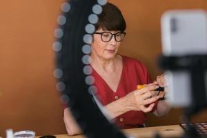 Middle-aged woman talking on cosmetics with makeup eye shadows and blush palette and brushes while recording her video. Mature female making video for her blog on cosmetics photo