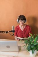Mature woman making podcast recording for her online show. Attractive business woman using headphones front of microphone for a radio broadcast photo