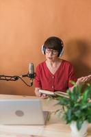 Mature woman making podcast recording for her online show. Attractive business woman using headphones front of microphone for a radio broadcast photo