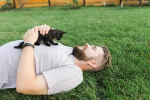 hombre con gatito acostado y jugando en la hierba - amistad amor animales y concepto de dueño de mascota foto