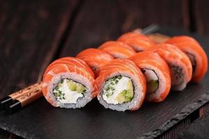 Sushi roll philadelphia with salmon and cucumber with avocado and cream cheese on black background. Sushi menu. Japanese food concept photo