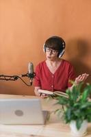 Portrait of mature woman wearing headphones and talking at online radio station - podcast and broadcast concept photo