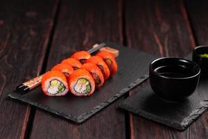 rollo de sushi de california con cangrejo, aguacate, pepino y caviar tobiko servido en el primer plano de la pizarra - comida japonesa foto