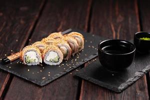 cocina japonesa - rollo de sushi con pepino y queso crema cubierto con un primer plano de anguila en una pizarra negra foto