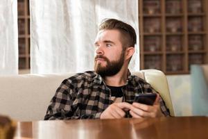 Young hipster guy looking news from social networks read via smartphone on free time in cafe photo